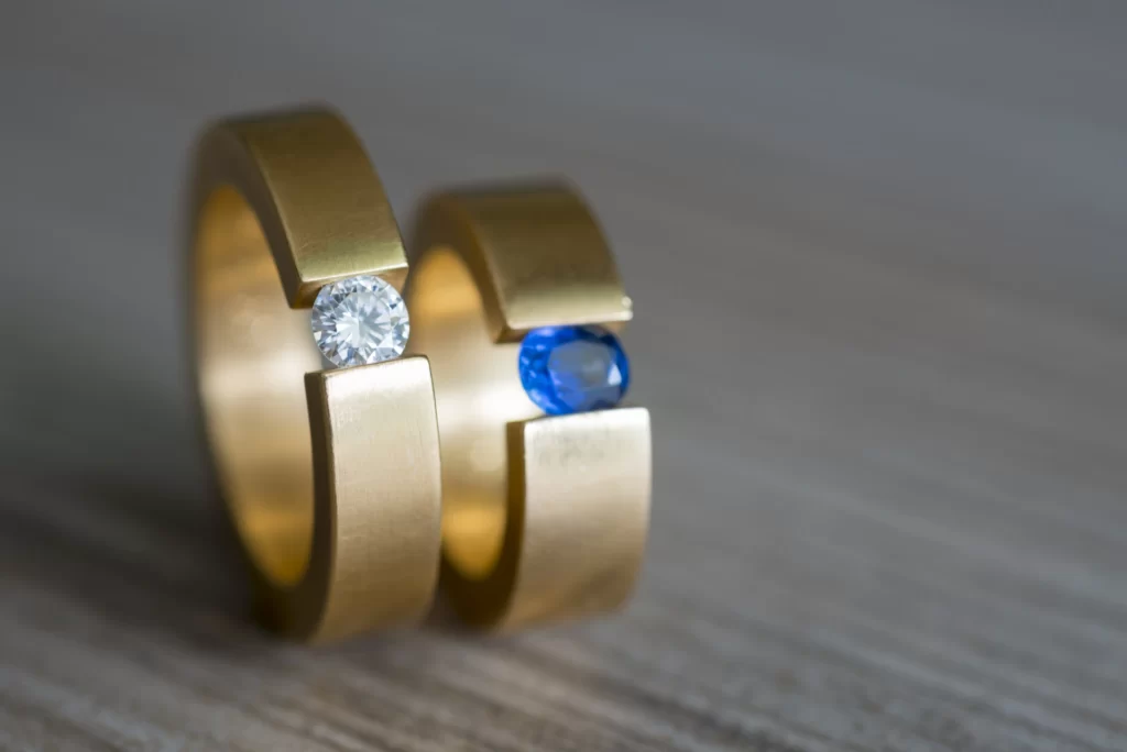 A side-by-side of two rings with birthstones and matching designs.