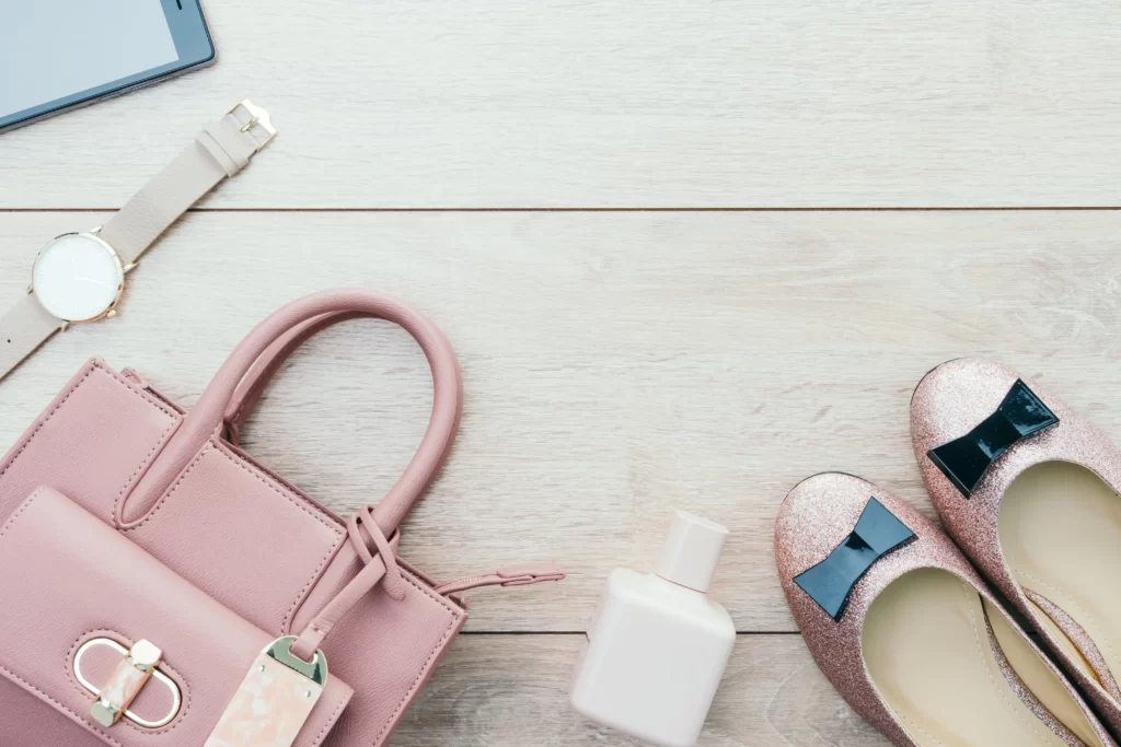 Flat lay of wedding shower outfit accessories, including a clutch bag, earrings, sunglasses, and perfume.